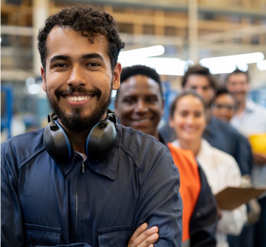 A man smiles with headphones around his shoulder as several people stand behind him in a line. They are also smiling